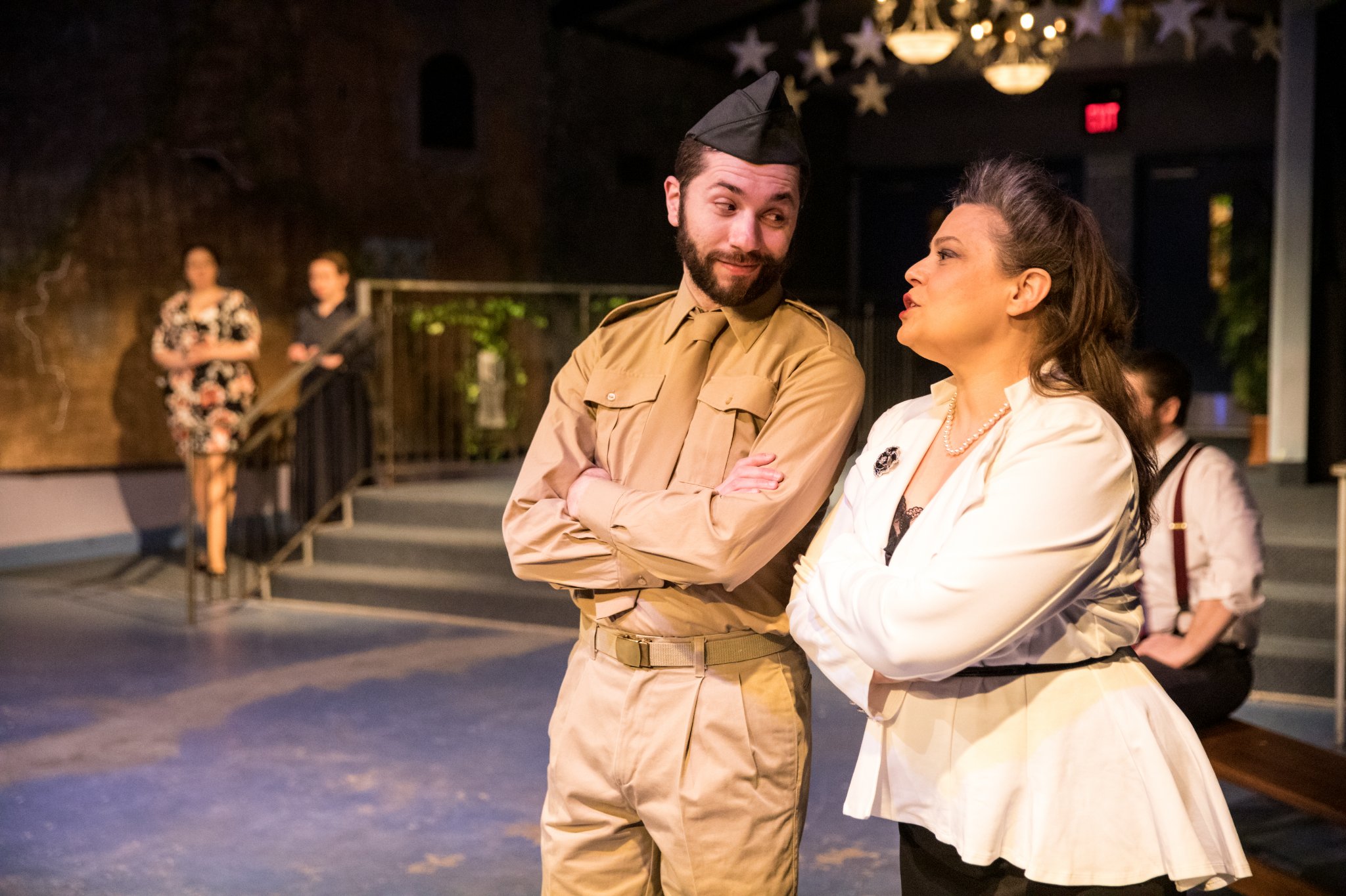 Bryce Kalal is wearing '40s-inspired army outfit while speaking to a woman, his co-star on stage.