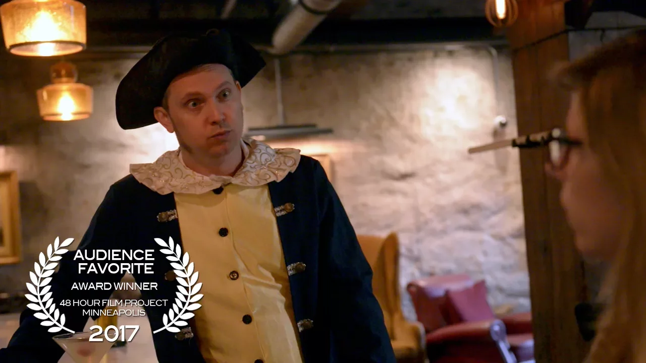 A man in a revolutionary era costume has a surprised face while he speaks to a woman in a bar. A text overlay reads "Audience Favorite Award Winner: 48 Hour Film Project, Minneapolis, 2017."