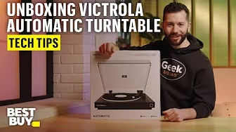 A YouTube thumbnail of Bryce Kalal wearing a Geek Squad sweatshirt standing next to a white box. Text reads: "Unboxing Victrola Automatic Turntable. Tech Tips."